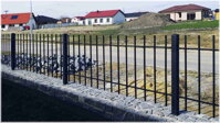 černý kovaný plot tvořenými probíjenými prvky, instalovaný mezi zabetonované kovové sloupky