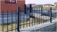 instalace černého kovového plotu s probíjenými prvky, v pozadí se vstupní brankou
